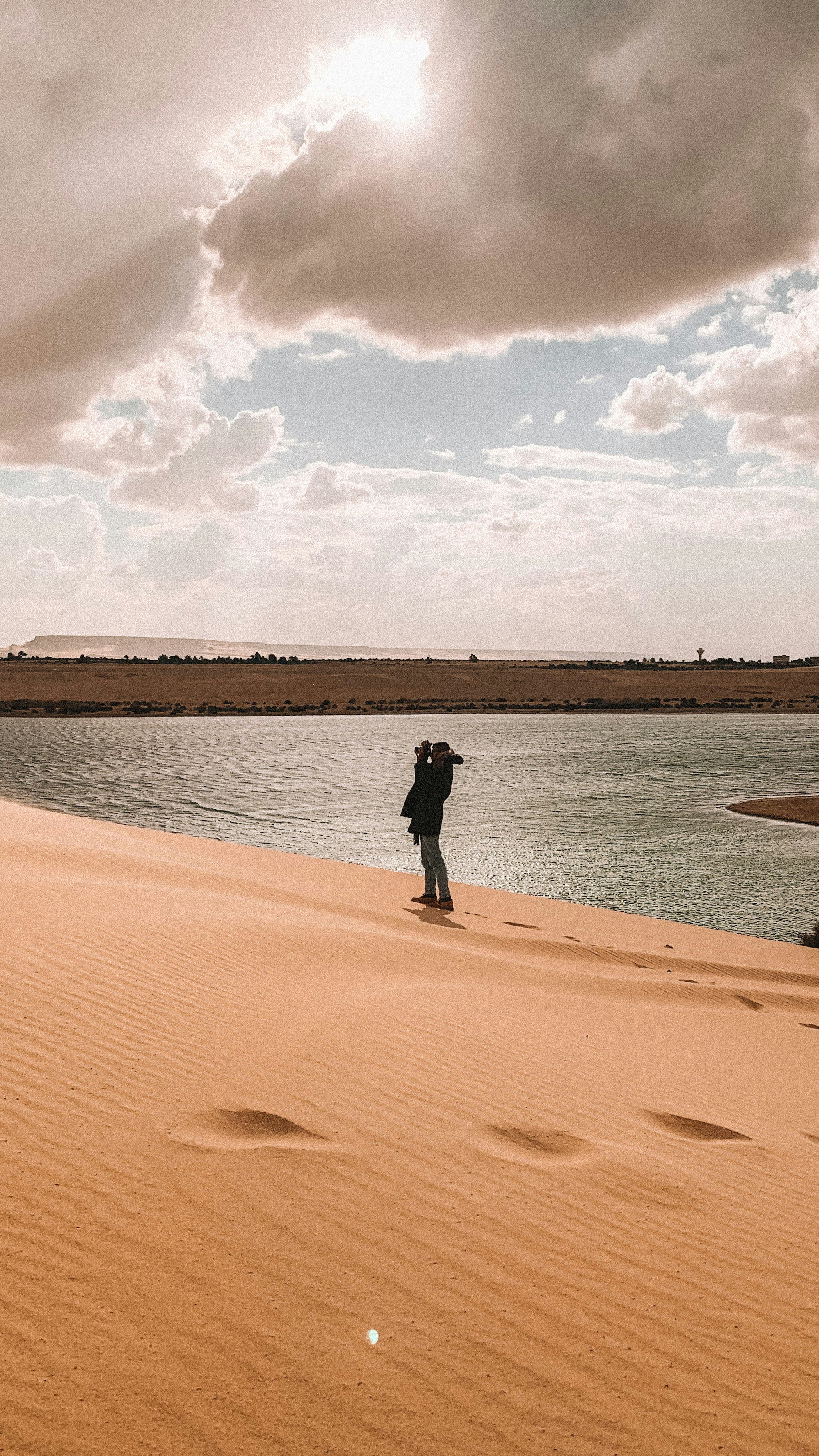 man in black jacket standing on brown sand near body of water during daytime
